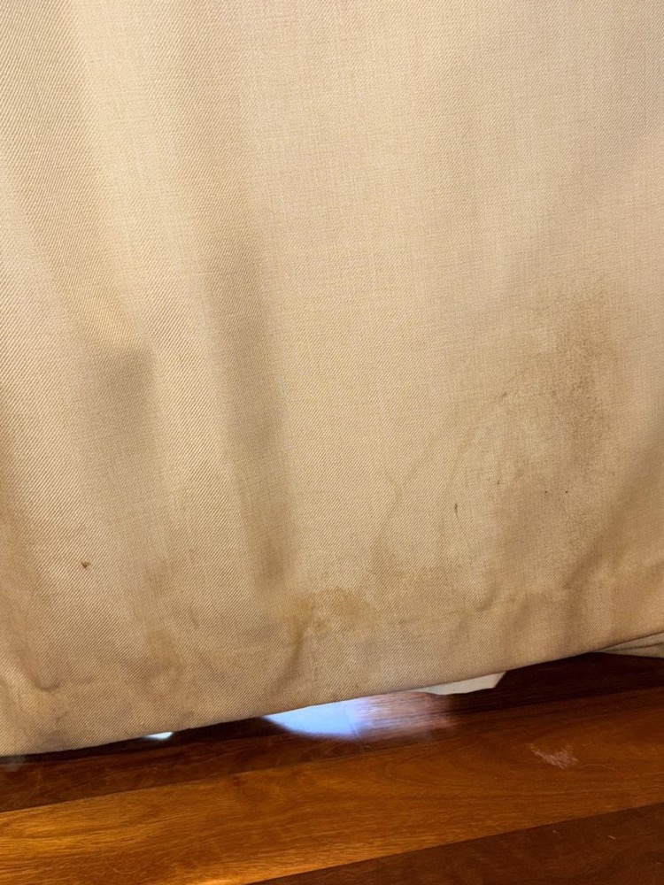 Beige curtain hem with dark brown stains before cleaning