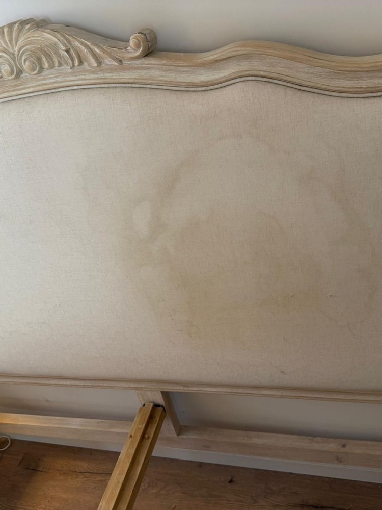 Upholstered headboard with a visible stain ring before fabric cleaning